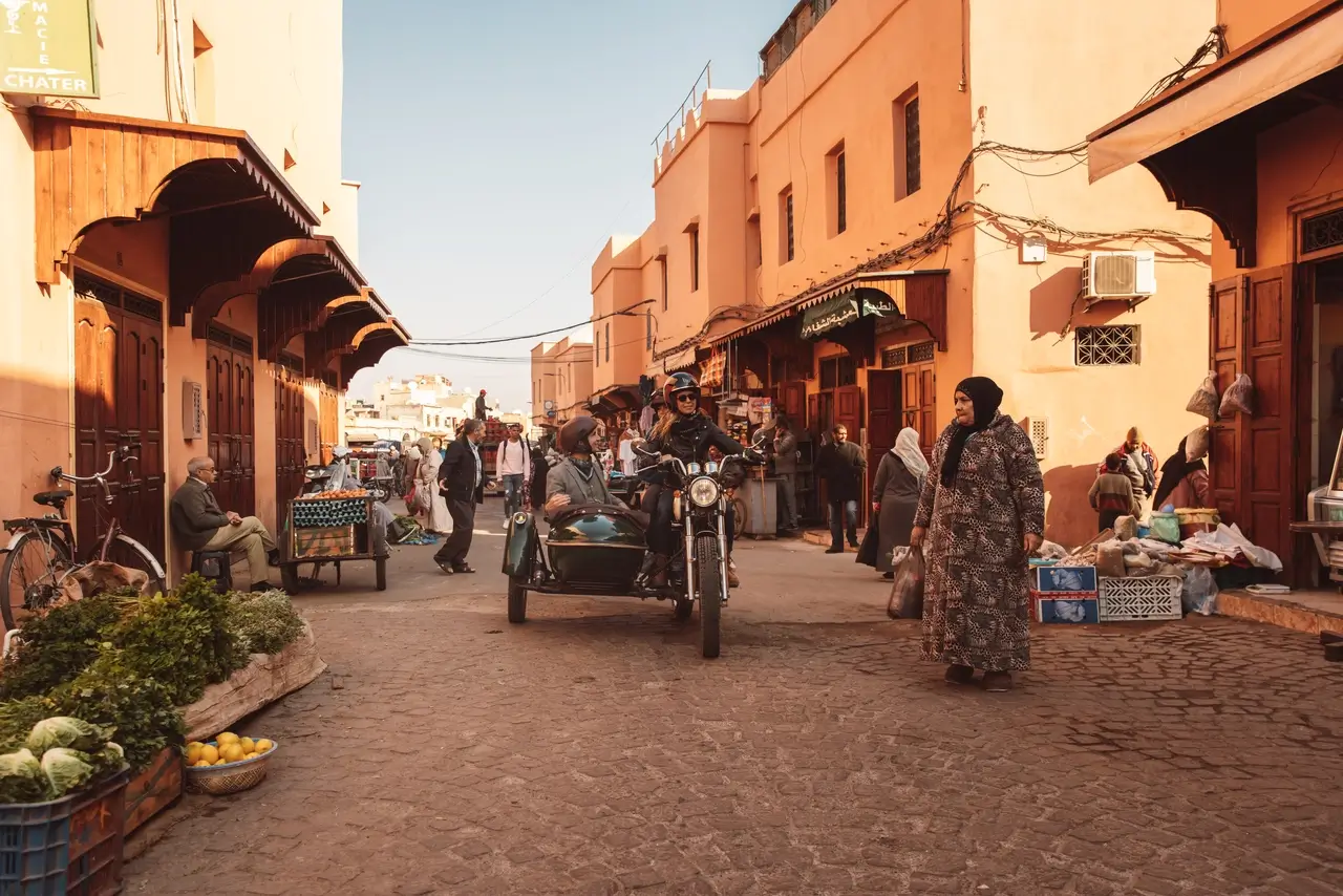 Side-car passing through a busy Marrakech street lined with market stalls