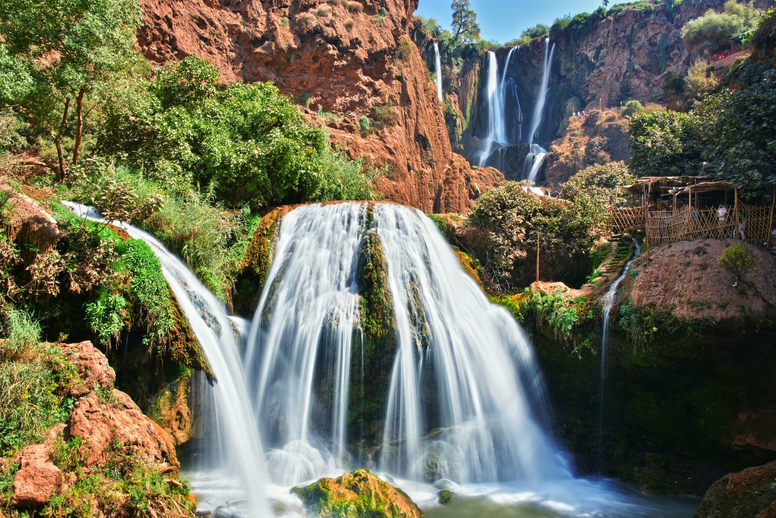 Ouzoud Waterfalls tumbling into a turquoise pool surrounded by olive trees and lush greenery